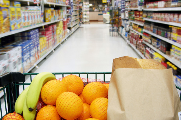 Grocery cart loaded with fresh fruit and bread moving through the aisle.